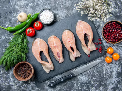 top-view-raw-fish-slices-black-board-vegetables-knife-pomegranate-seeds-table_179666-46547